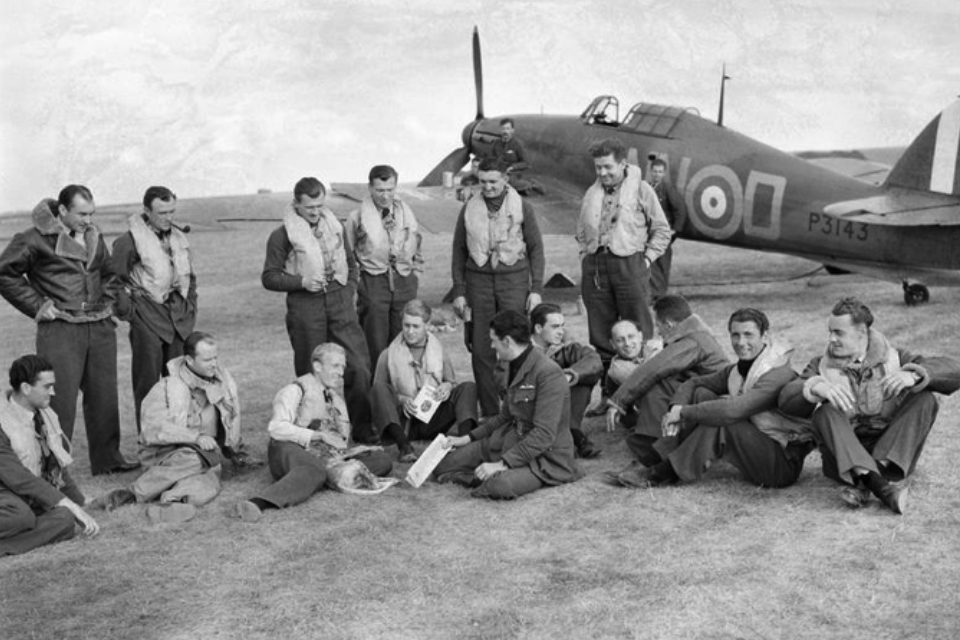 No. 310 (Czech) Squadron are grouped together informally. Most of the men are wearing their life jackets and a Spitfire is stationed in the background. 